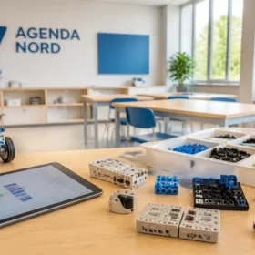 Un piccolo robot didattico modulare poggiato su un banco da laboratorio STEM in legno. Sullo sfondo sfocato si vede lo schermo di un laptop con un'interfaccia colorata per la programmazione a blocchi.